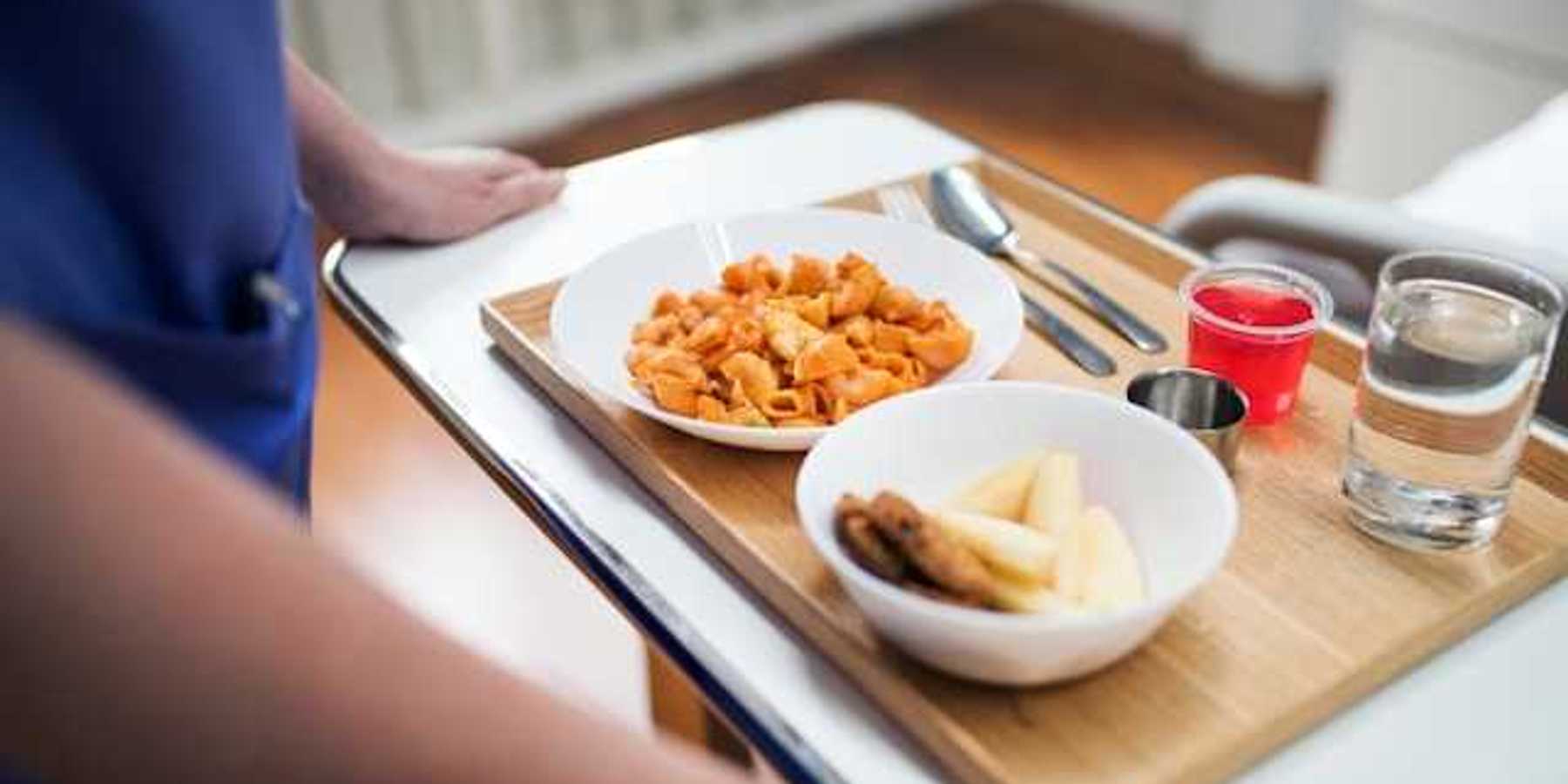 A person holding a tray with a hospital meal on it