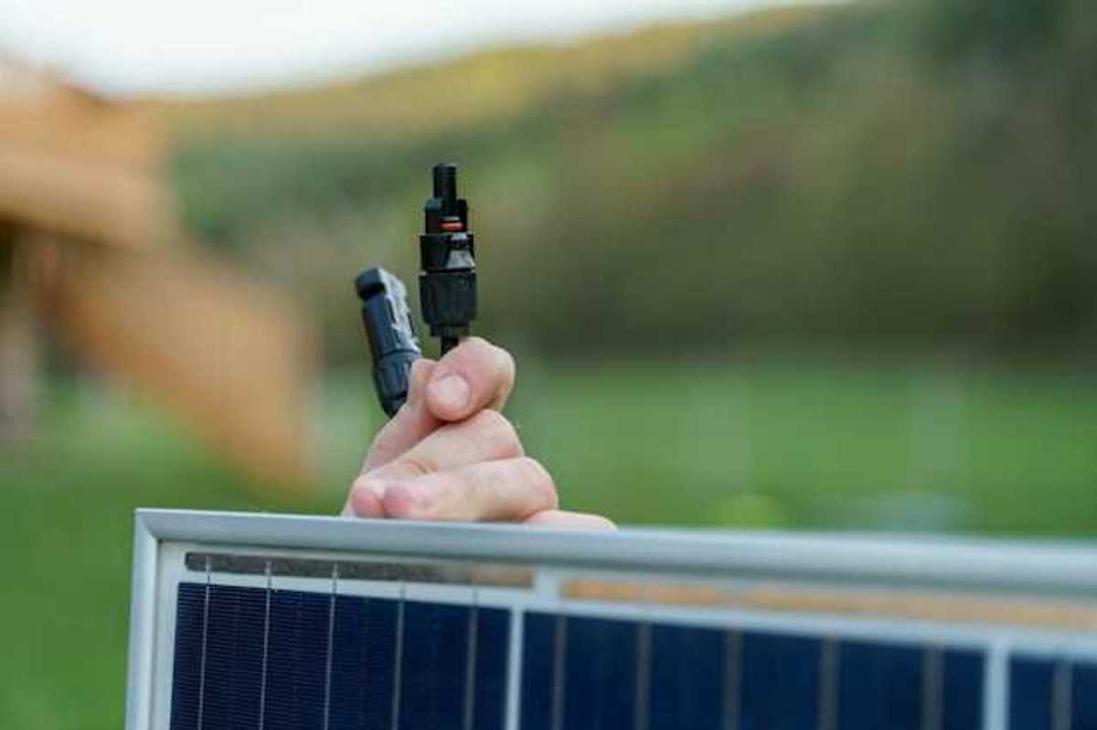 A person holding on to a small solar panel with plugs in their hand