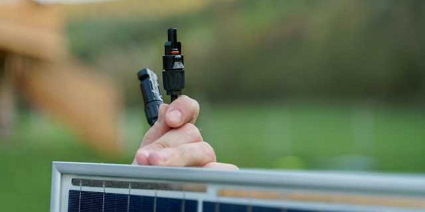 A person holding on to a small solar panel with plugs in their hand