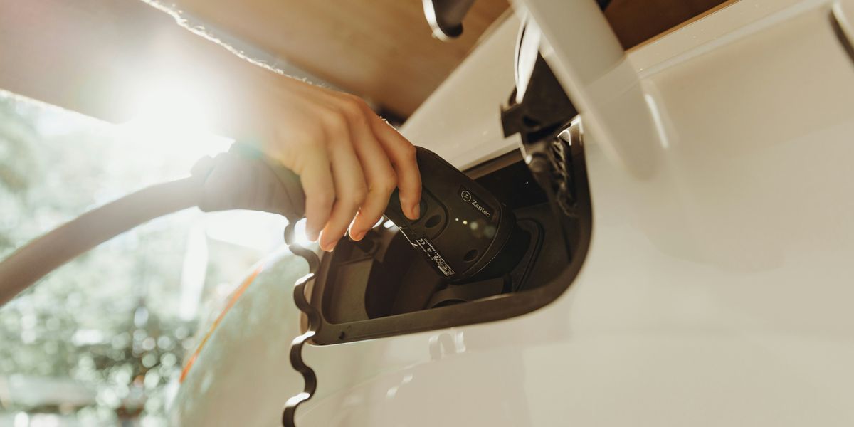 A person inserting a charger into a white electric vehicle.