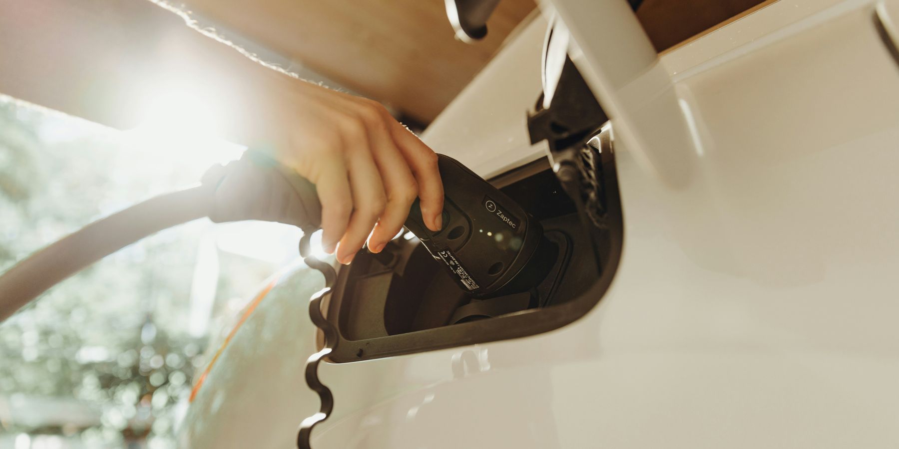 A person inserting a charger into a white electric vehicle.