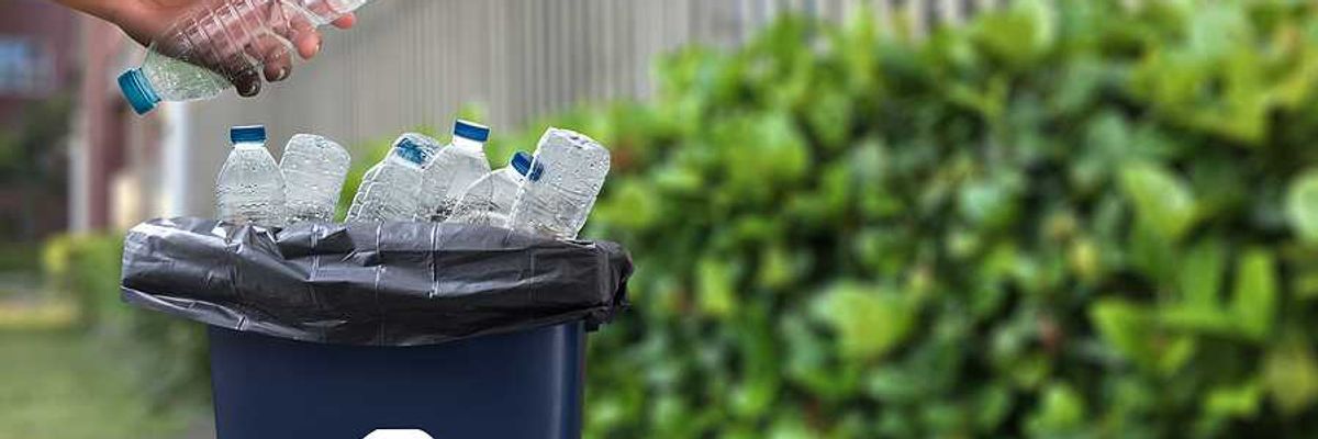 A person putting a plastic water bottle into a recycling container