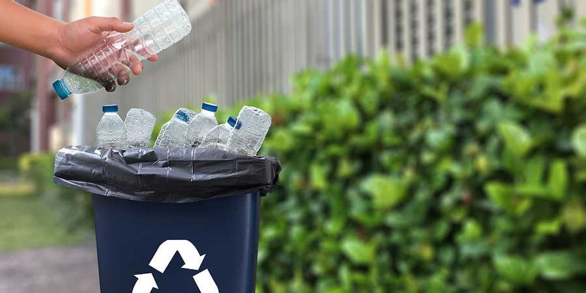 A person putting a plastic water bottle into a recycling container