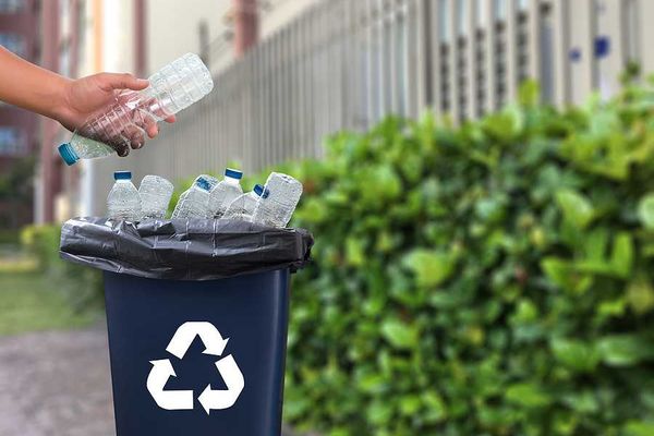 A person putting a plastic water bottle into a recycling container