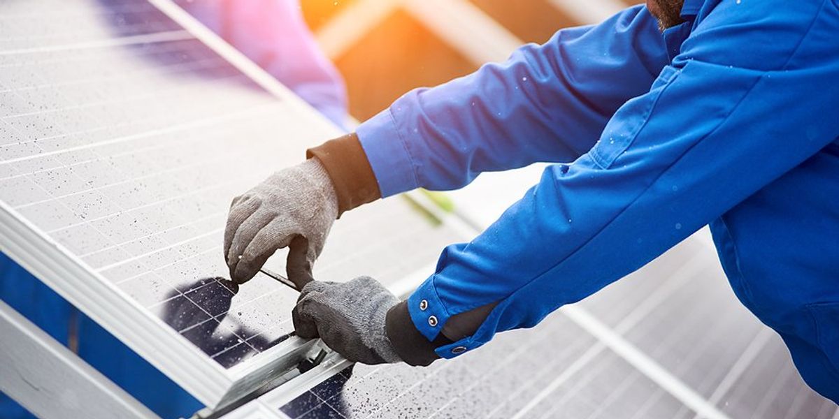 A person's gloved hands installing solar panels on a roof.