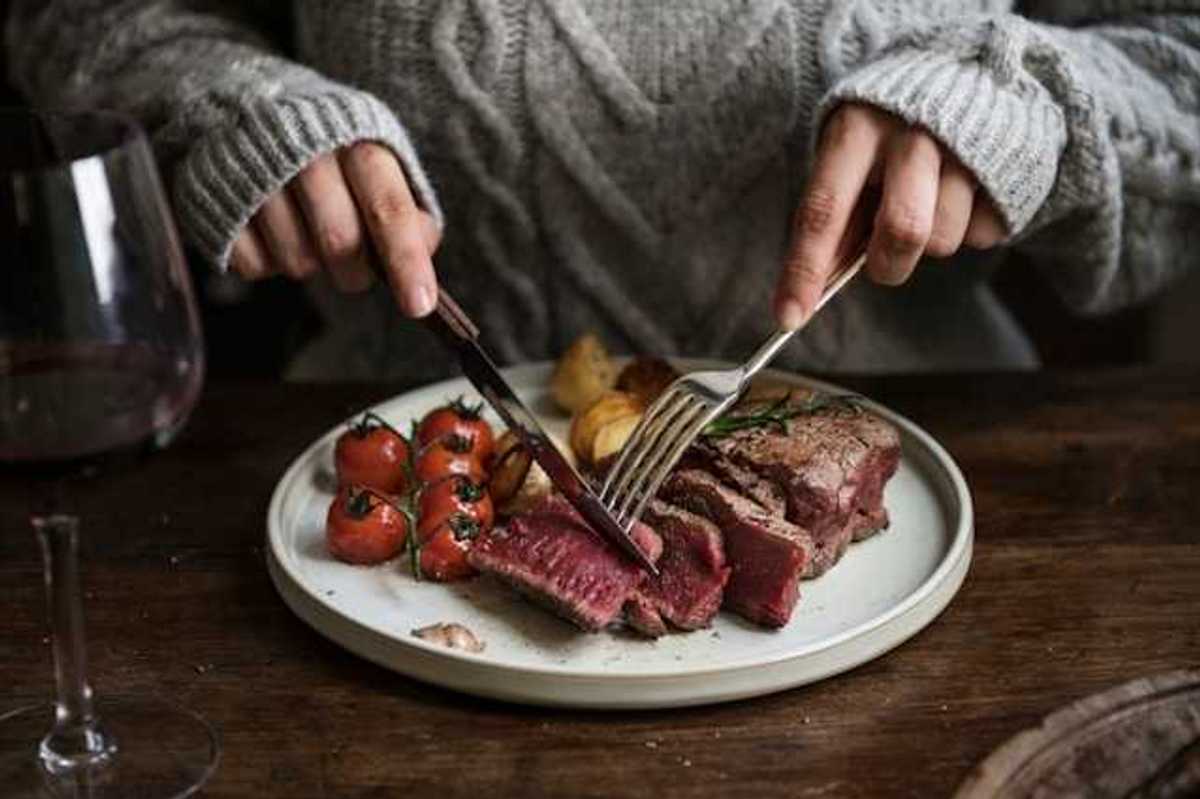 A person sitting at a table cutting into a cooked steak on a plate