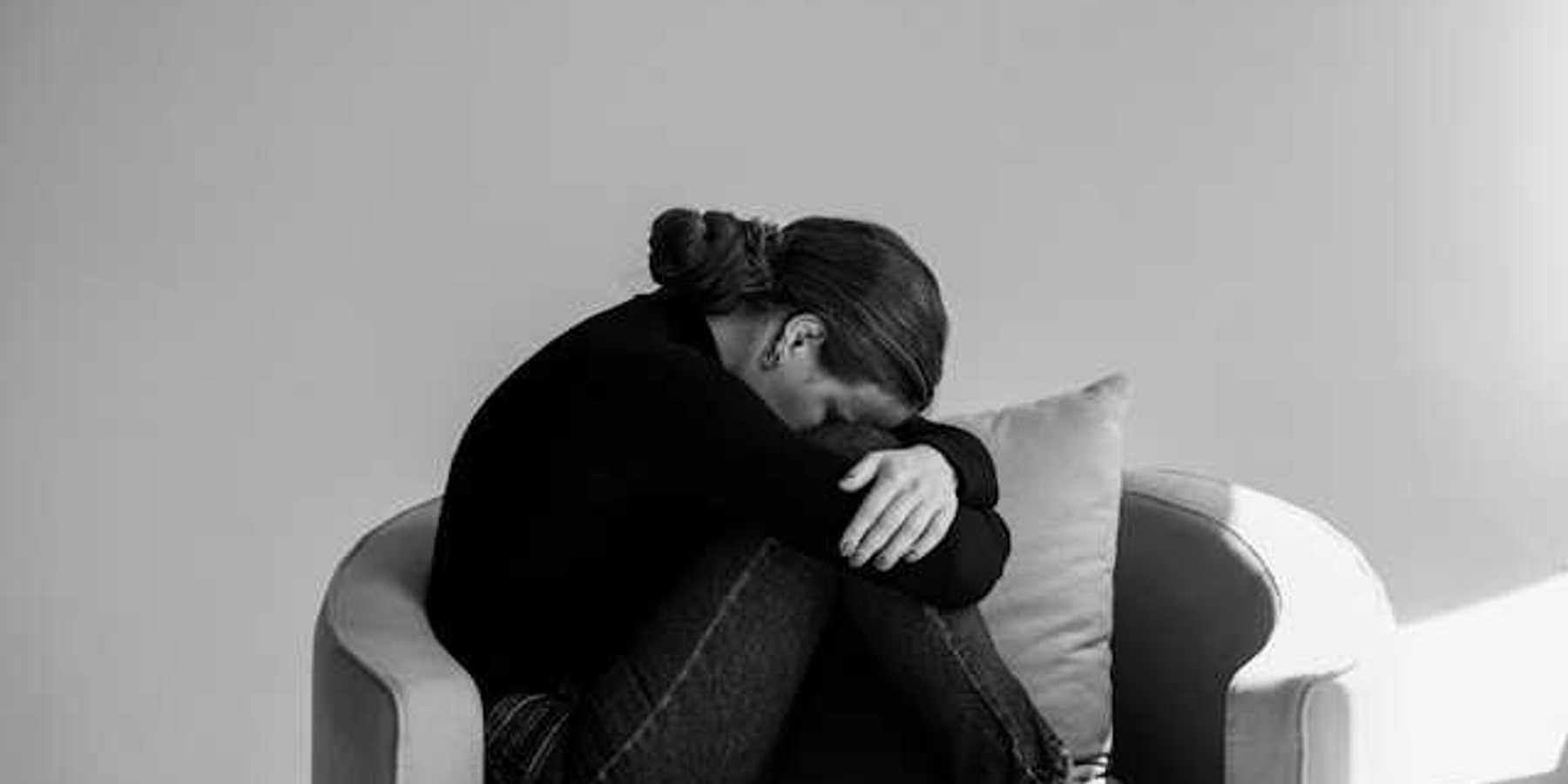 A person sitting in a chair with their head on their knees