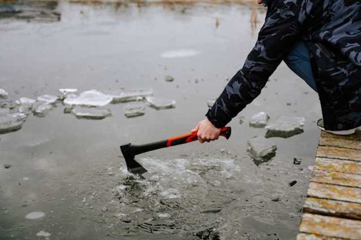 A person sitting on a dock breaking the ice on a lake