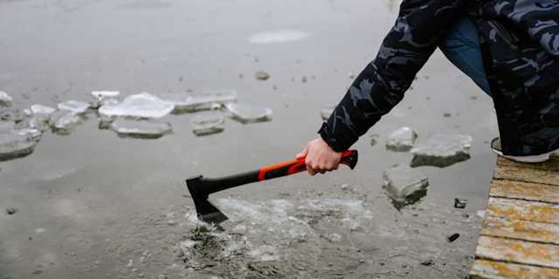 A person sitting on a dock breaking the ice on a lake