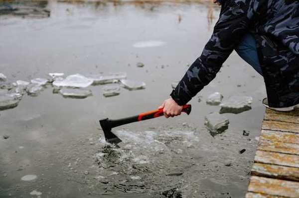A person sitting on a dock breaking the ice on a lake