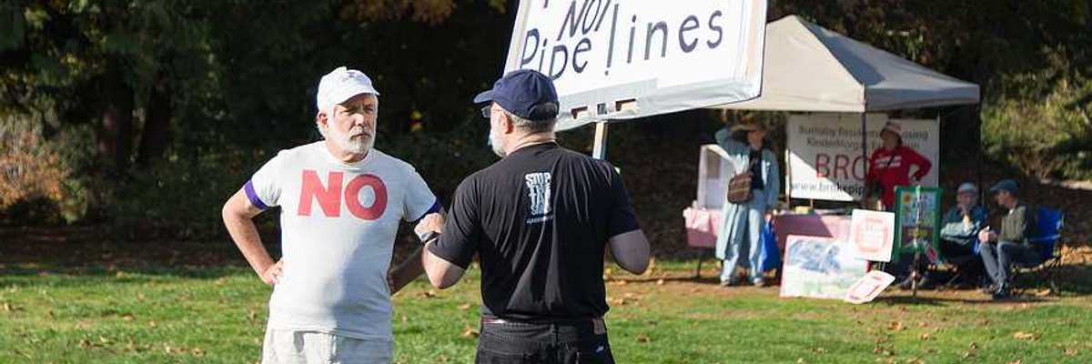 A person standing in a park with a sign saying 'picnics not pipelines'