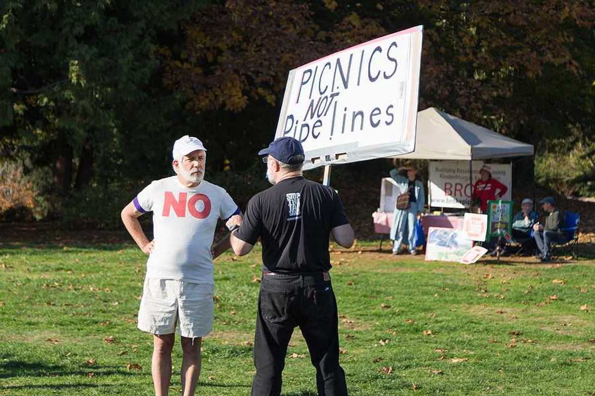 A person standing in a park with a sign saying 'picnics not pipelines'