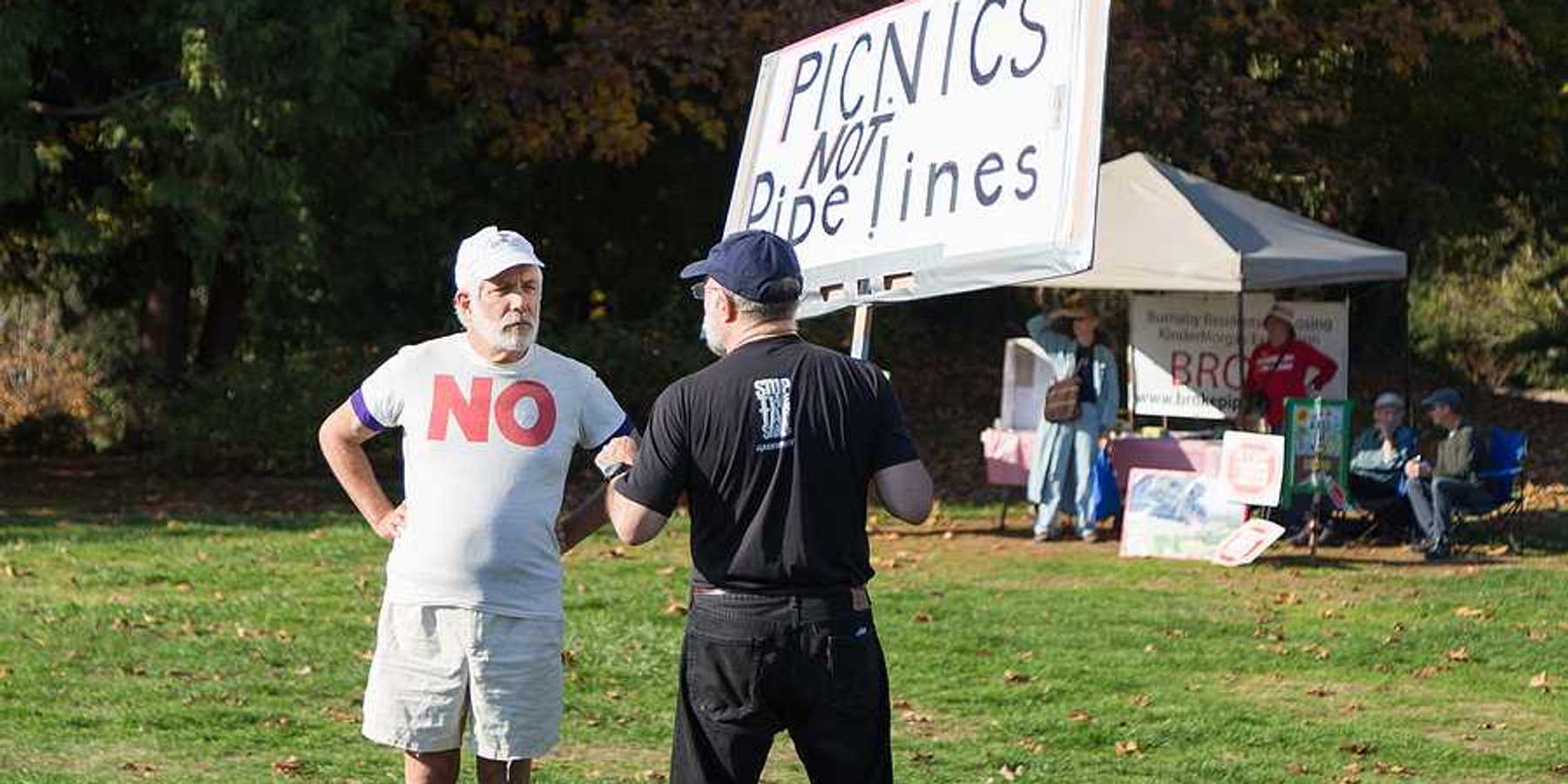 A person standing in a park with a sign saying 'picnics not pipelines'