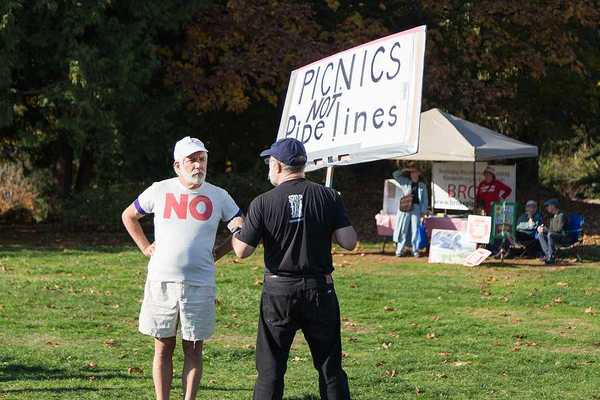 A person standing in a park with a sign saying 'picnics not pipelines'