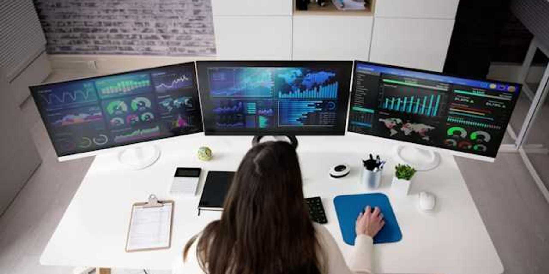 A person viewing three computer monitors with data on them