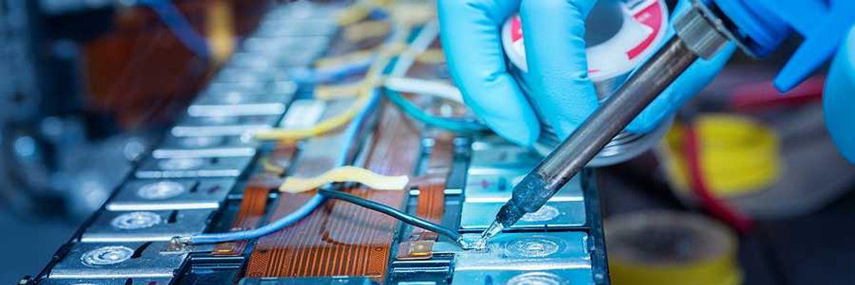A person wearing blue gloves soldering wire onto a lithium-ion battery