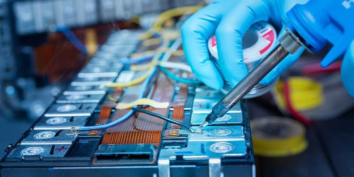 A person wearing blue gloves soldering wire onto a lithium-ion battery