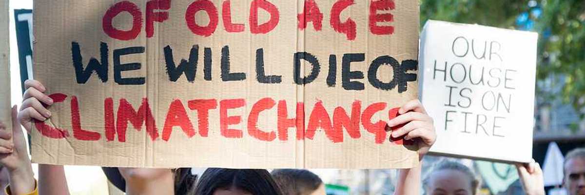 A person with a sign saying 'You will die of old age; we will die of climate change'