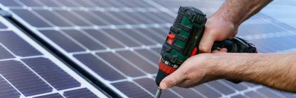 A person with cordless driver installing solar panels
