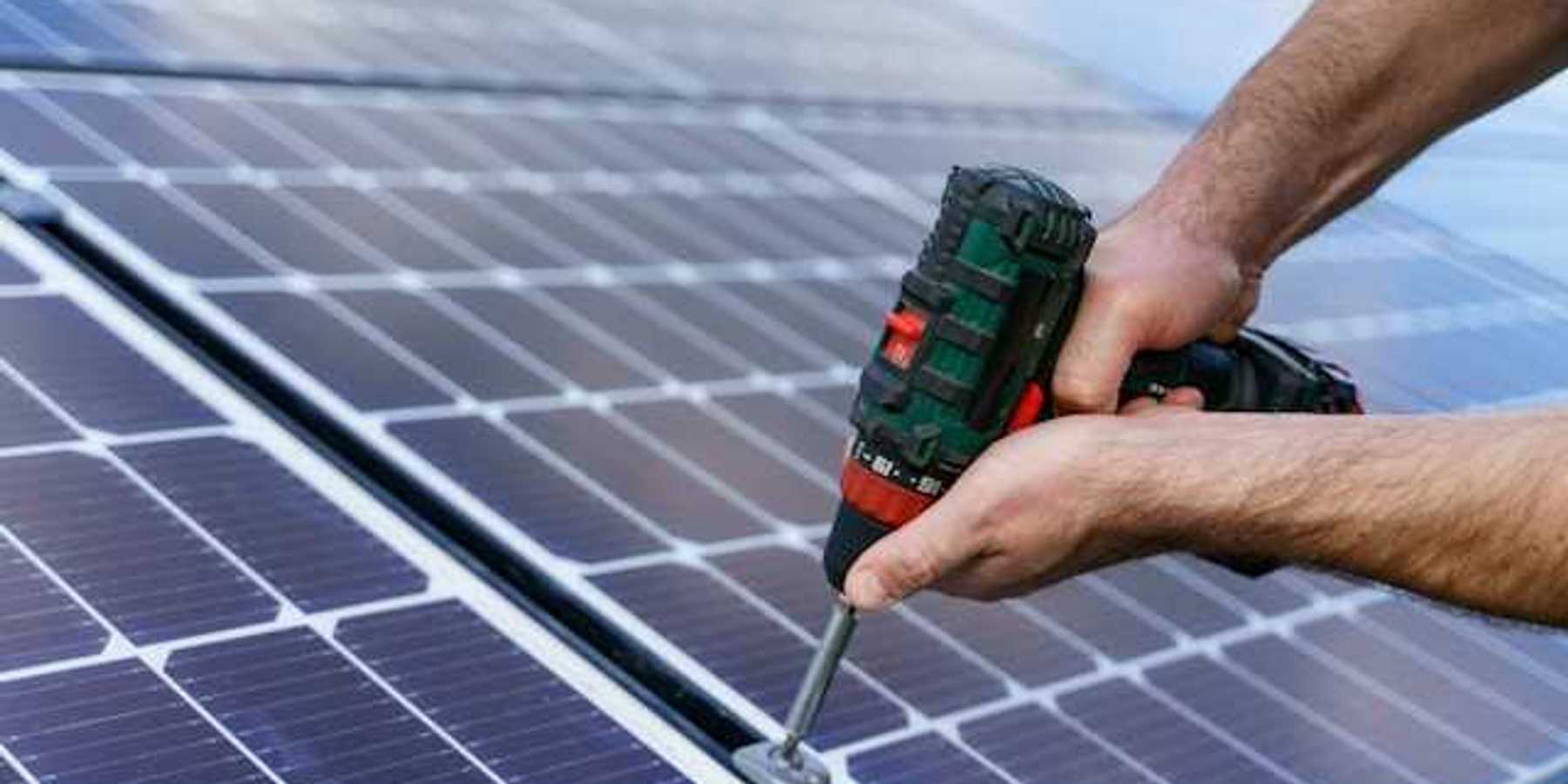 A person with cordless driver installing solar panels