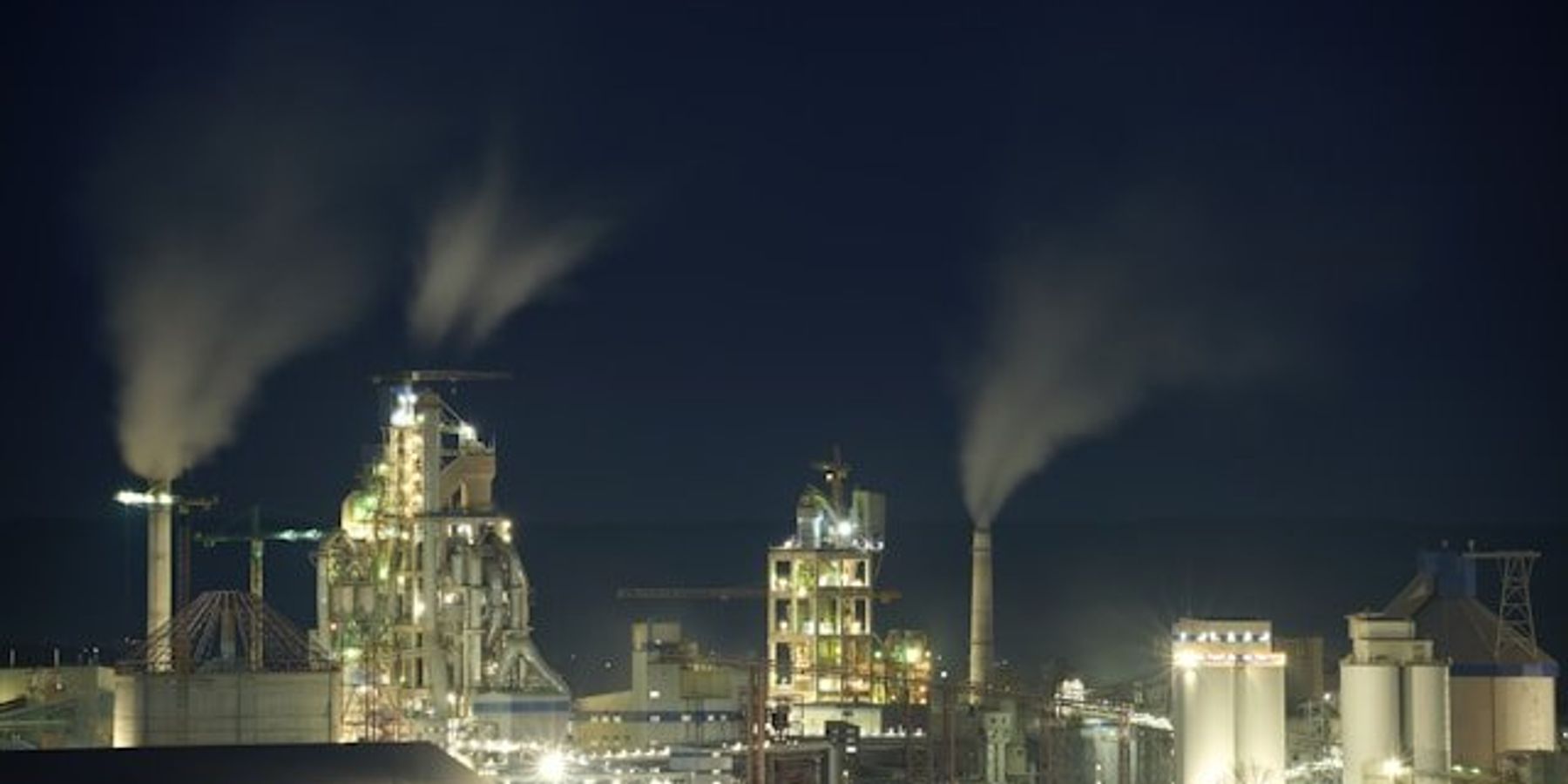 A petrochemical plant lit up at night with smoke billowing from chimneys.