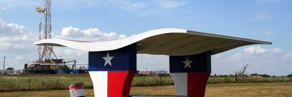 A picnic table at a Texas-motif rest stop with an oil rig in the background.