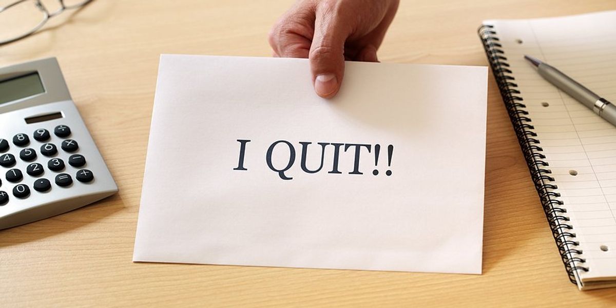 A piece of paper being passed across the desk with the words I Quit on it