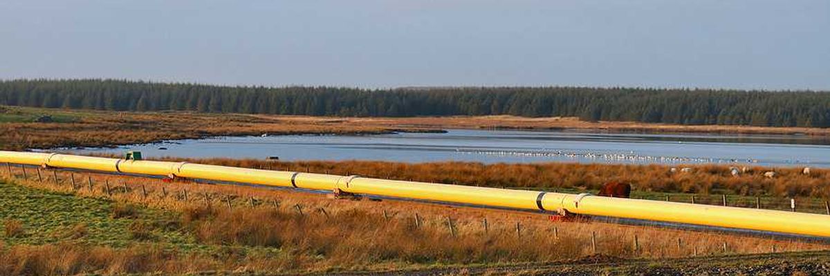A pipeline stretching across a wetlands area with a lake in the background