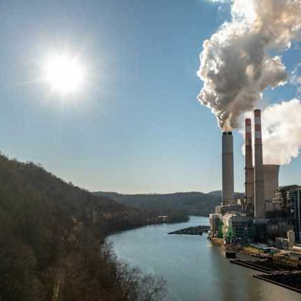 A power plant next to a river spewing smoke into the sky