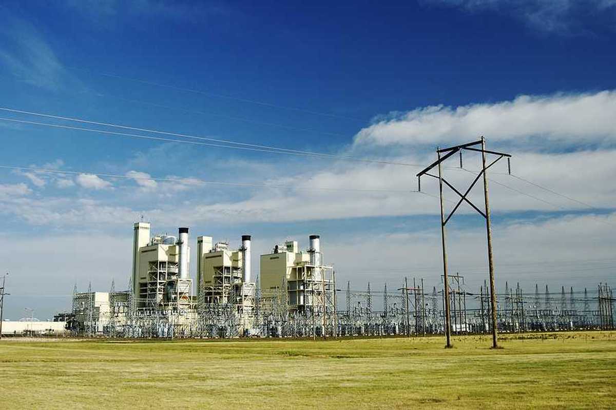 A power plant on a sunny day with a field in the foreground