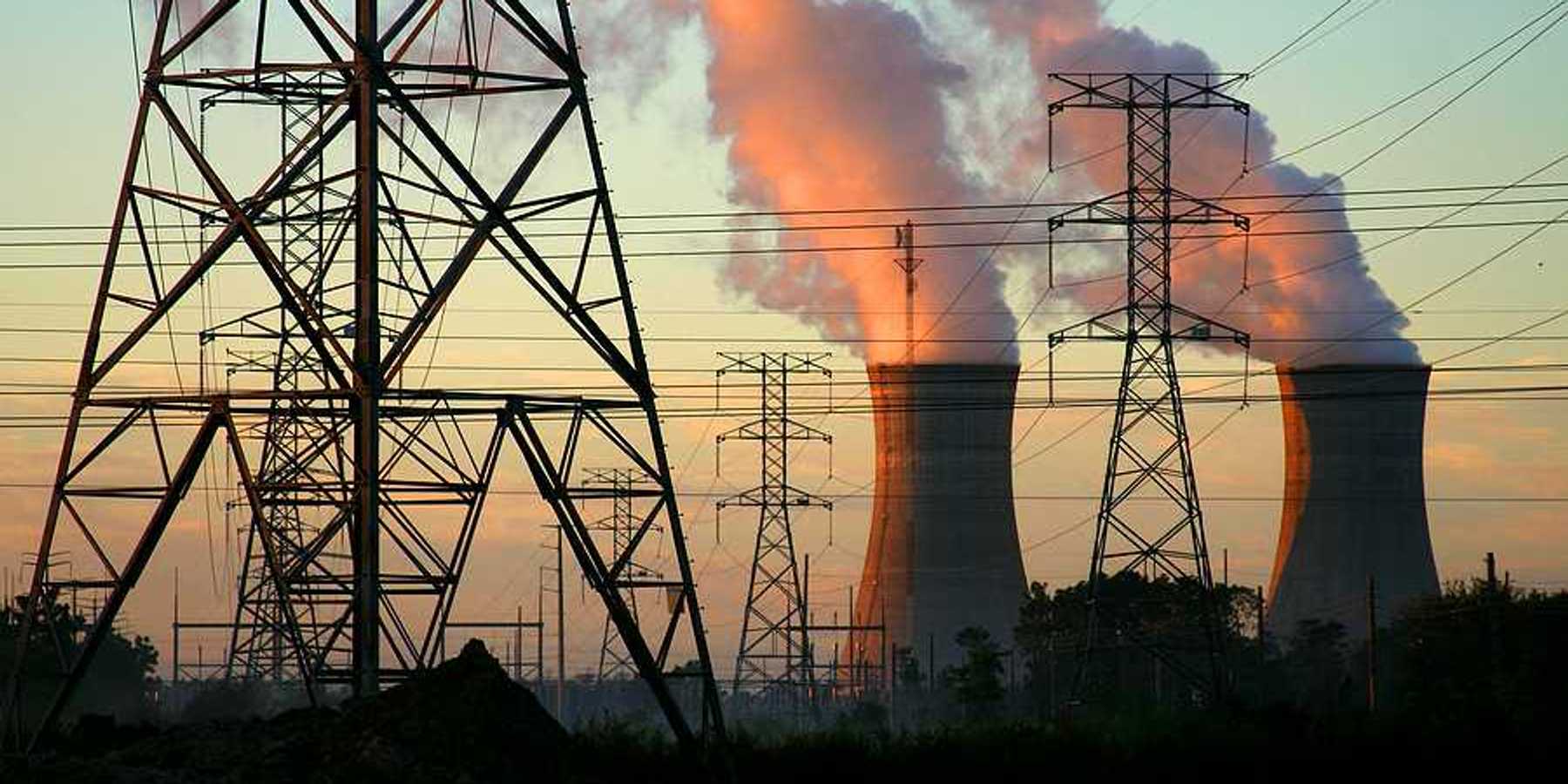 A power plant with smoke billowing from towers with electric energy lines in the foreground
