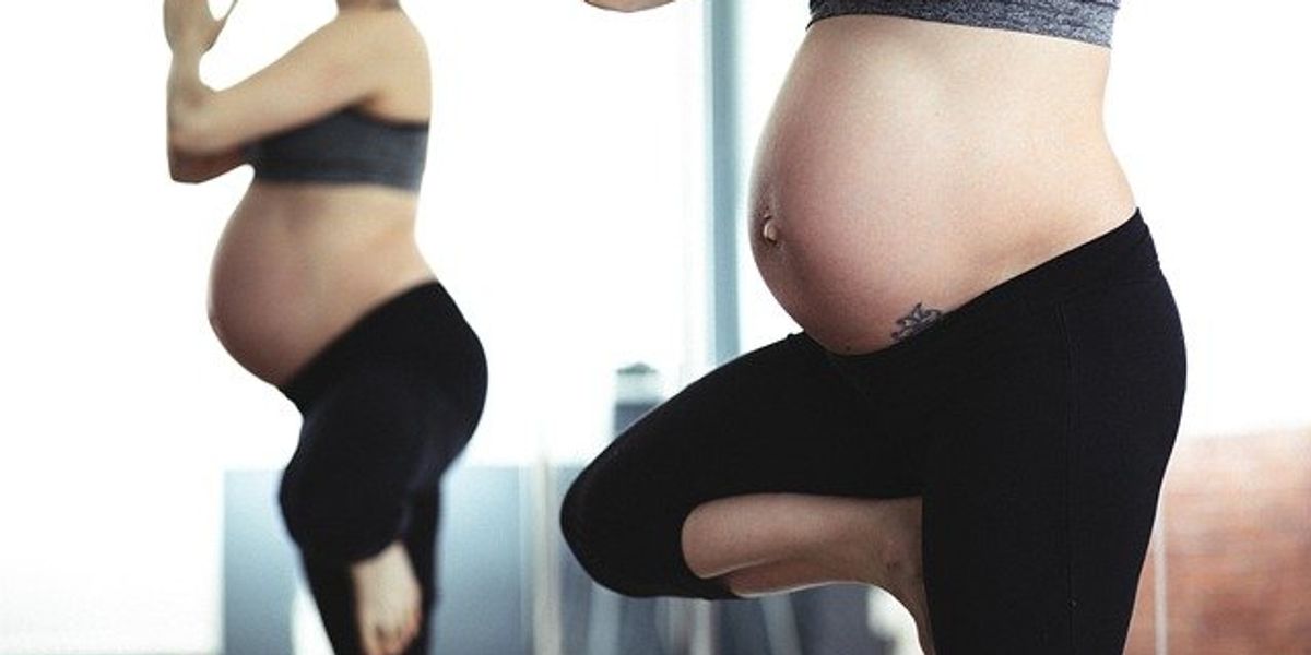 A pregnant woman in a yoga pose near a mirror