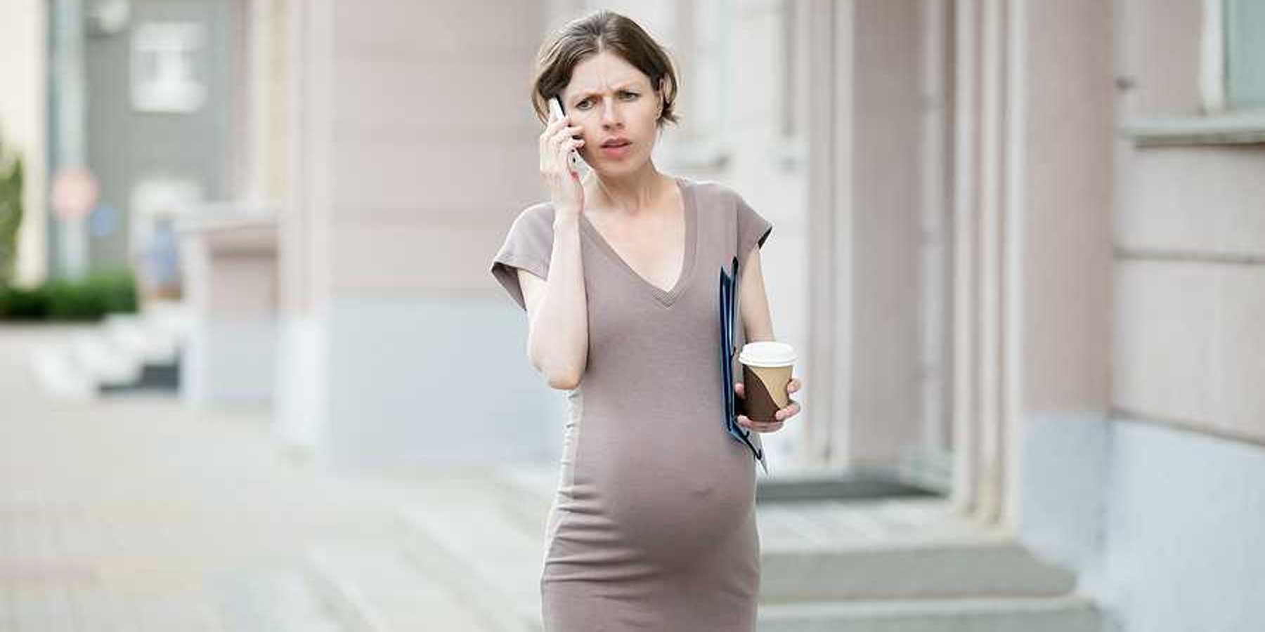 A pregnant woman walking down a street talking on the phone