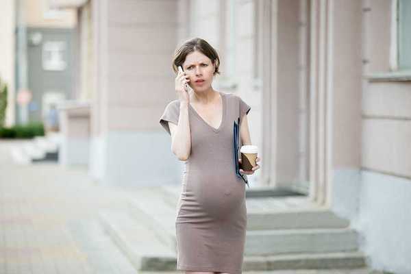 A pregnant woman walking down a street talking on the phone