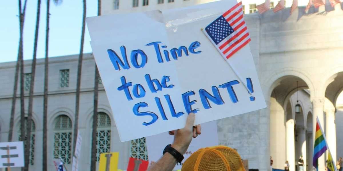 A protestor holds a sign "No time to be silent" during a Hands Off rally outside Los Angeles City Hall