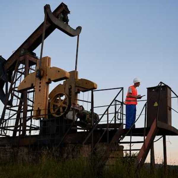 A pump jack with a maintenance worker on a platform next to it