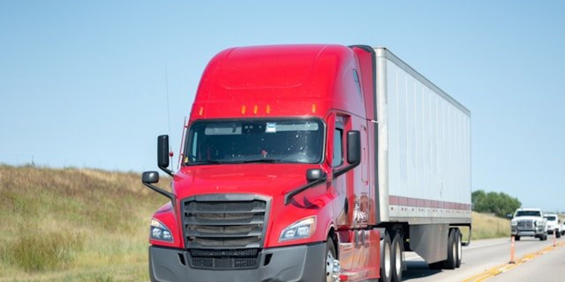 A red 18-wheeler truck on a highway.