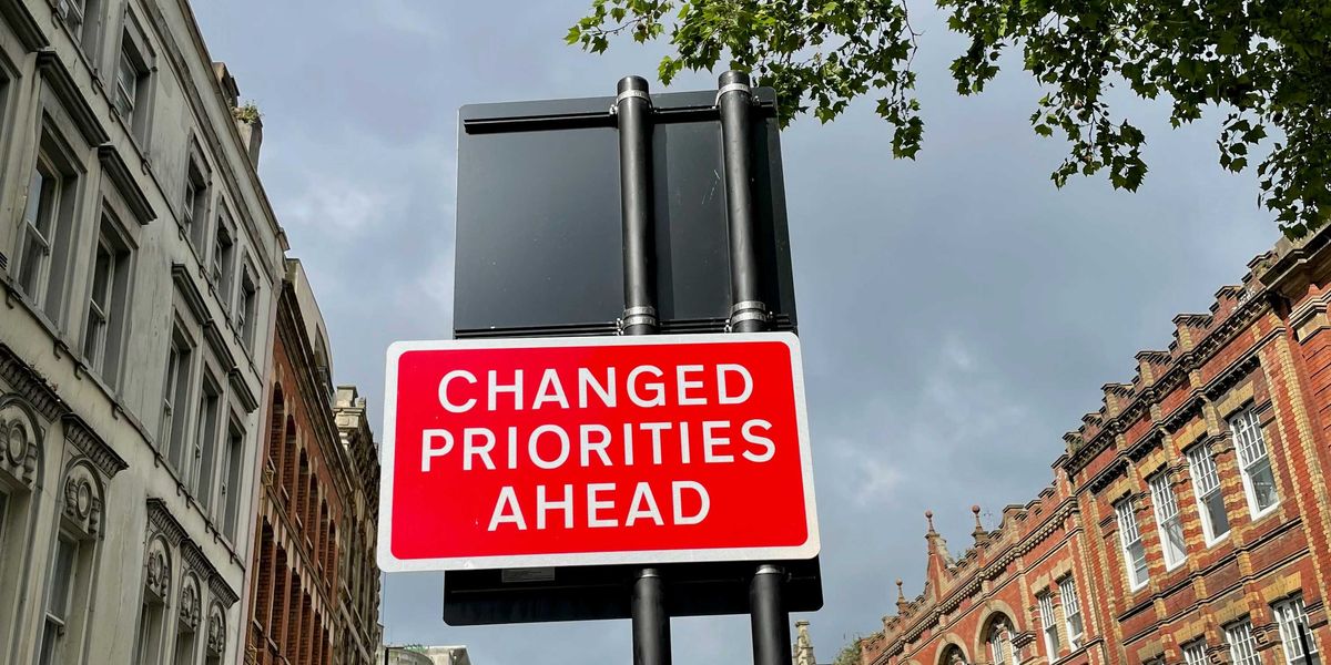 A red and white street sign saying Changed Priorities Ahead