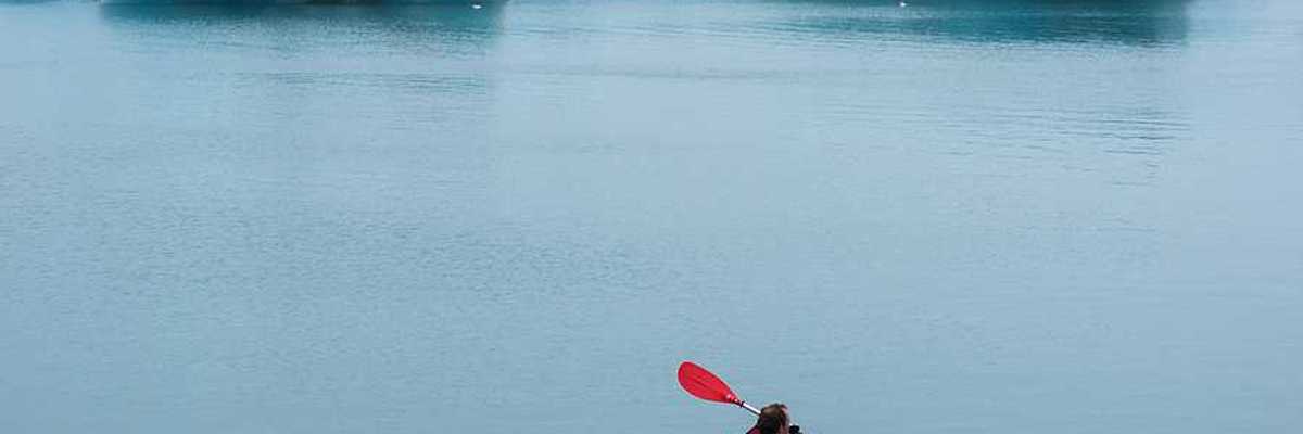 A red kayak with a person in it paddling past ice bergs