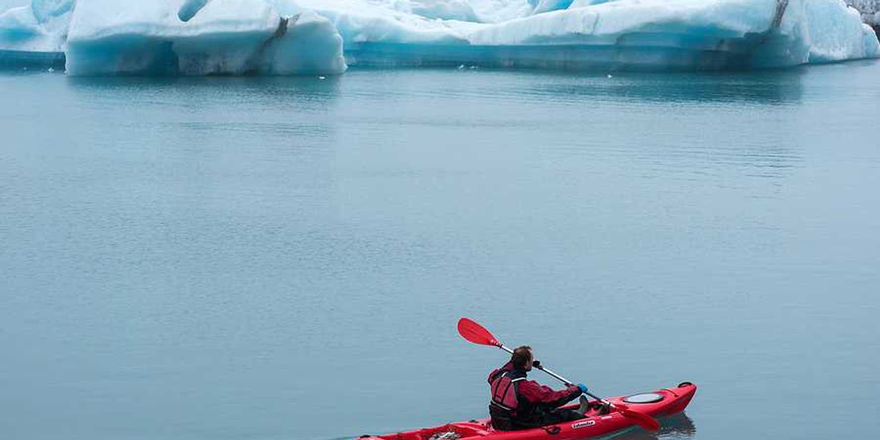 A red kayak with a person in it paddling past ice bergs