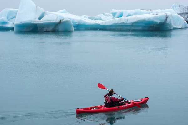 A red kayak with a person in it paddling past ice bergs