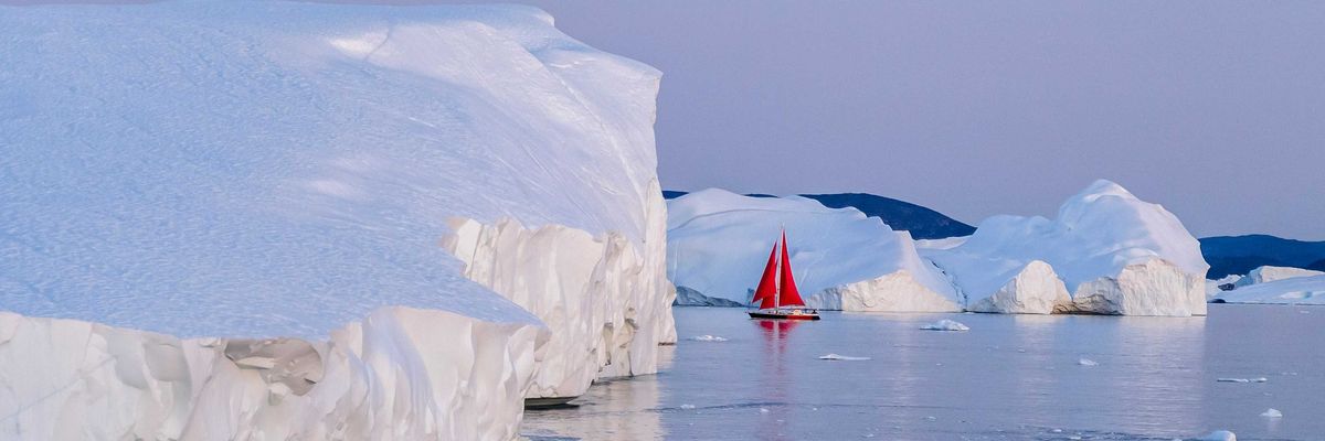 A red sailboat in the water near icebergs