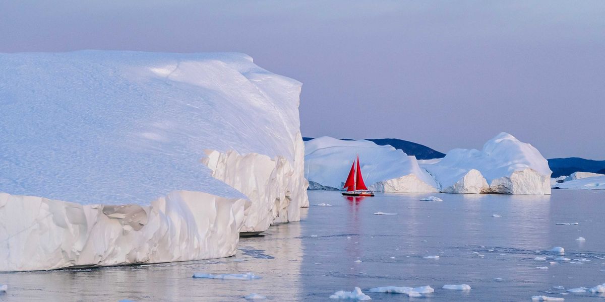 A red sailboat in the water near icebergs