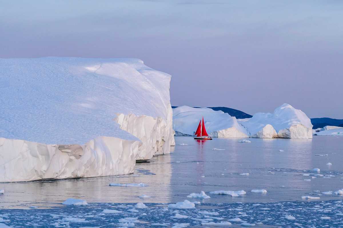 A red sailboat in the water near icebergs