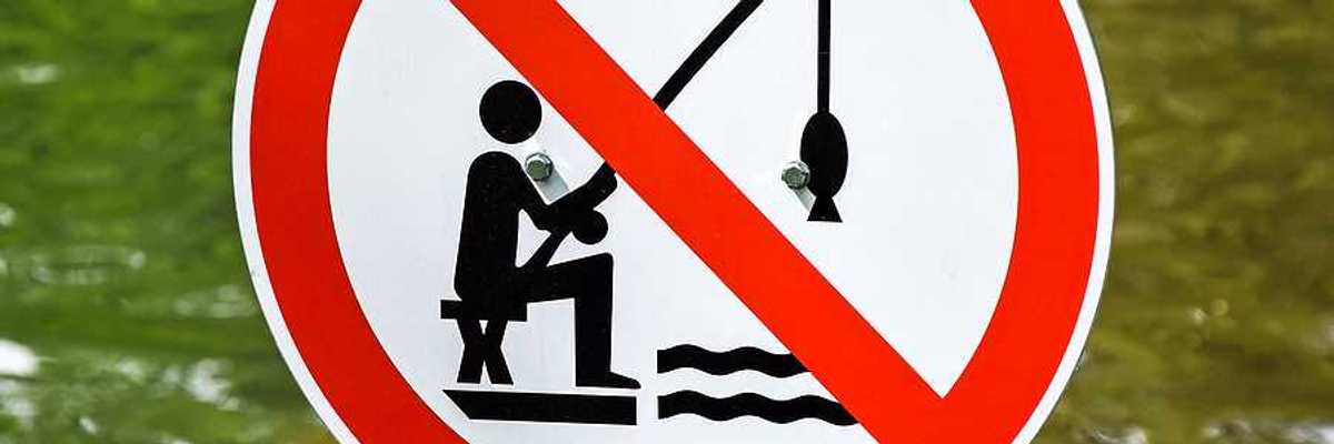 A red, white and black sign indicating that fishing is prohibited with a body of water in the background