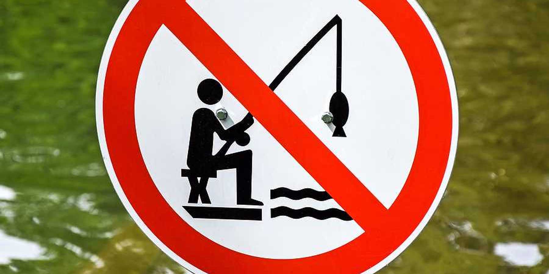 A red, white and black sign indicating that fishing is prohibited with a body of water in the background