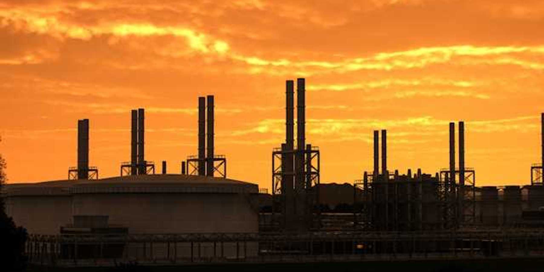 A refinery with smokestacks silhouetted against a sunset sky