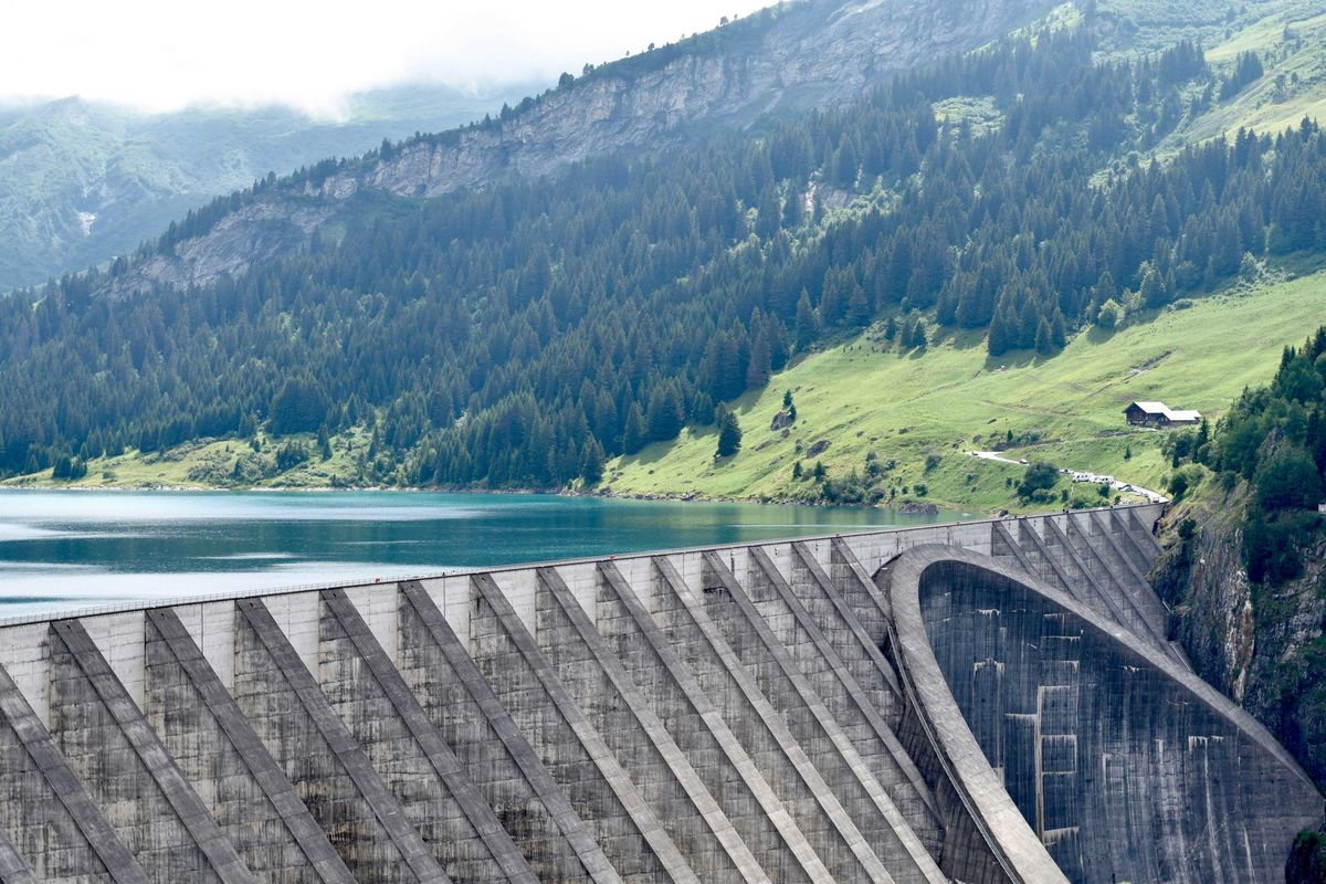 A reservoir with a dam with green mountains in the background