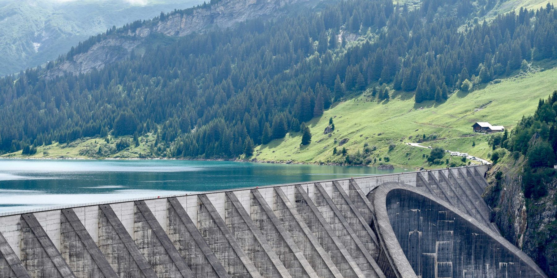 A reservoir with a dam with green mountains in the background