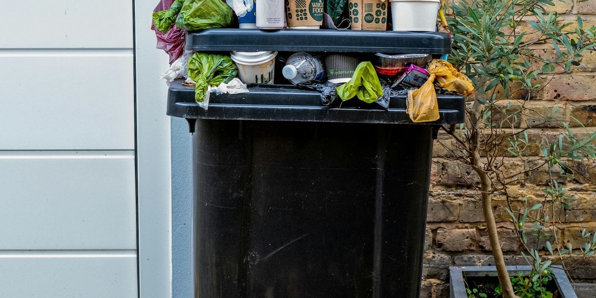 A residential garbage can overflows with plastic bottles and other waste.
